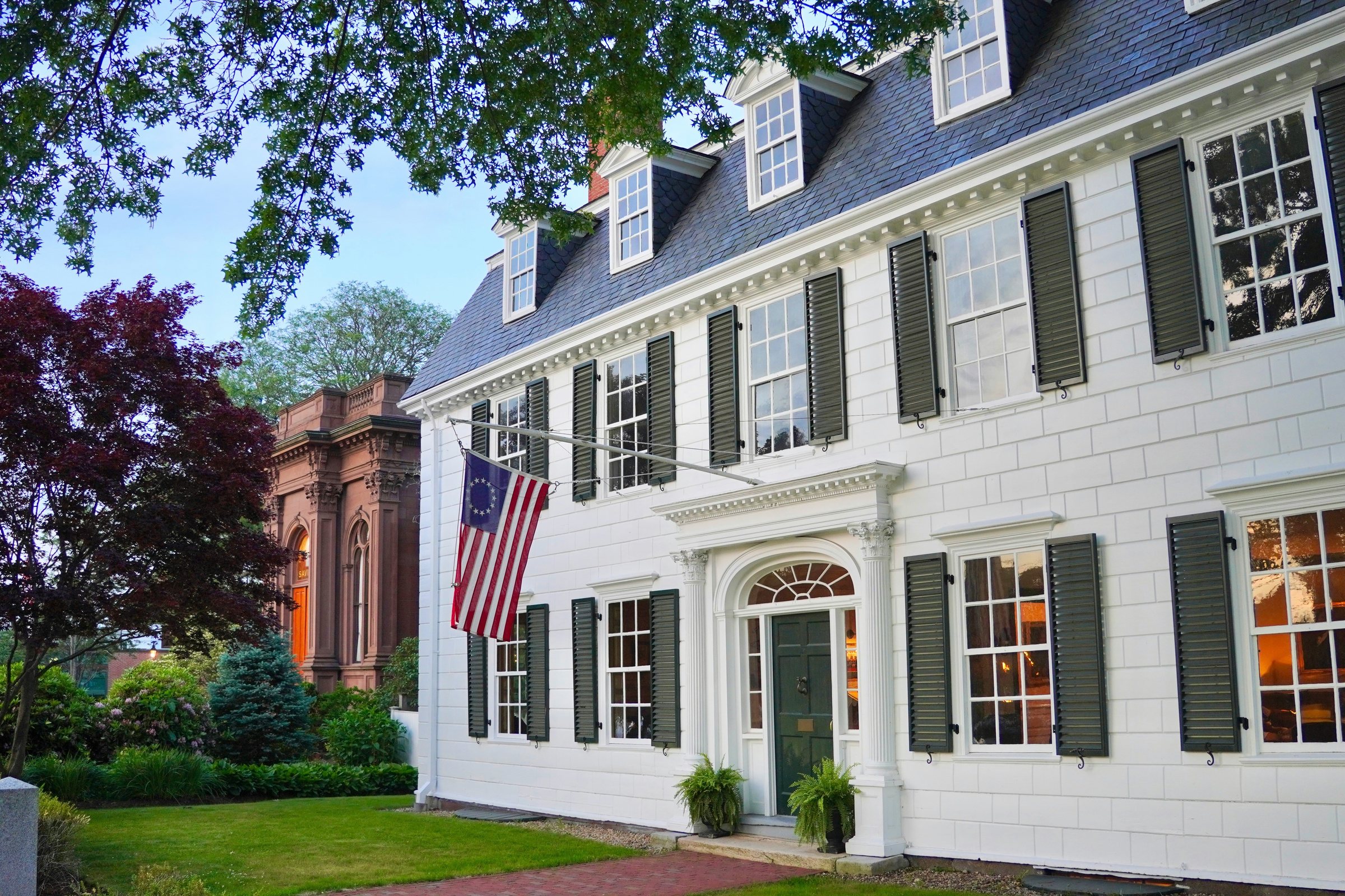A white colonial house with dark shutters and an American flag